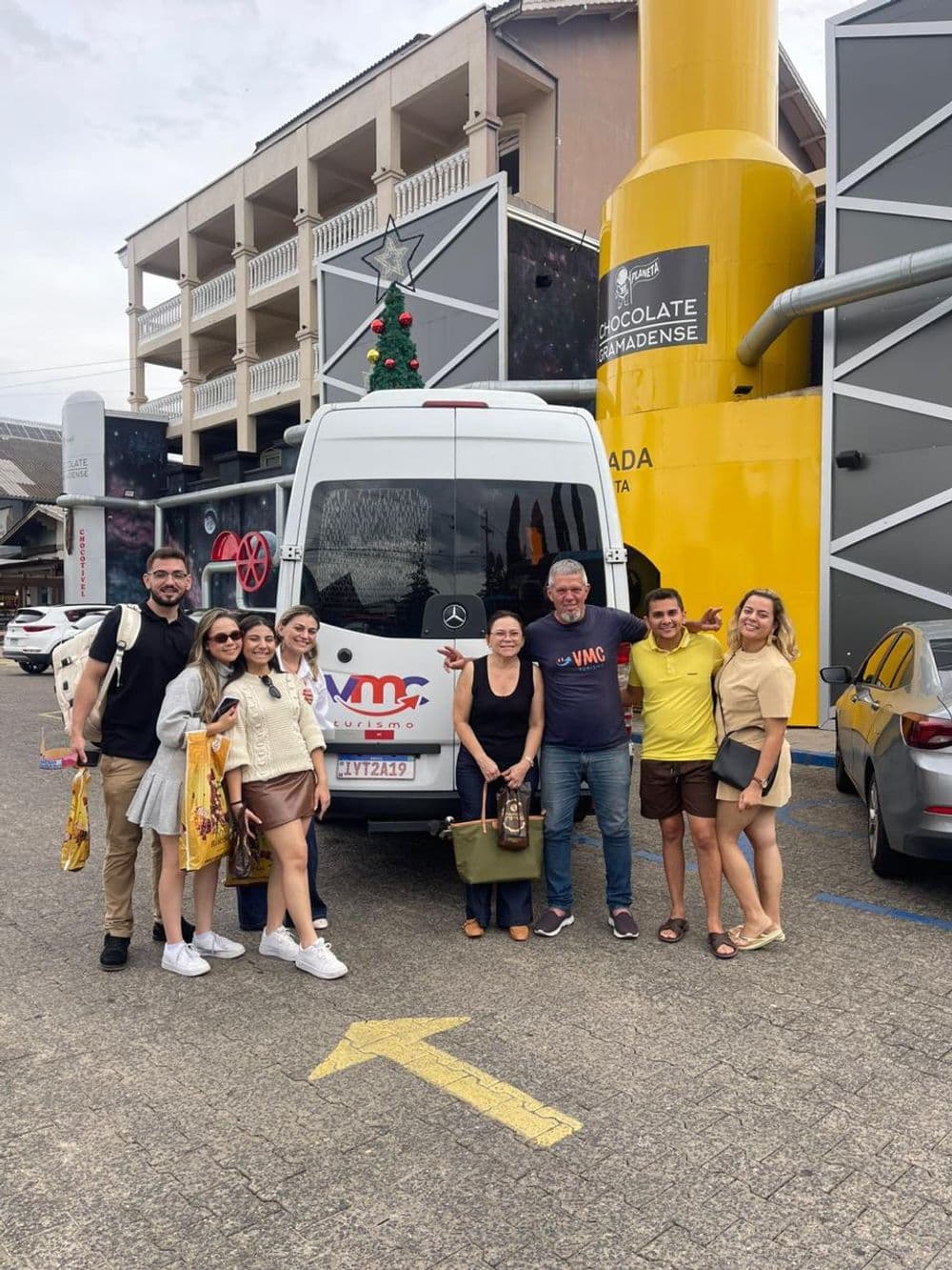Grupo de passageiros ao lado da van da VMC Turismo em frente à Chocolate Gramadense